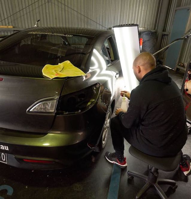 Man in a garage repairing a hail damaged vehicle using paintless dent removal techniques